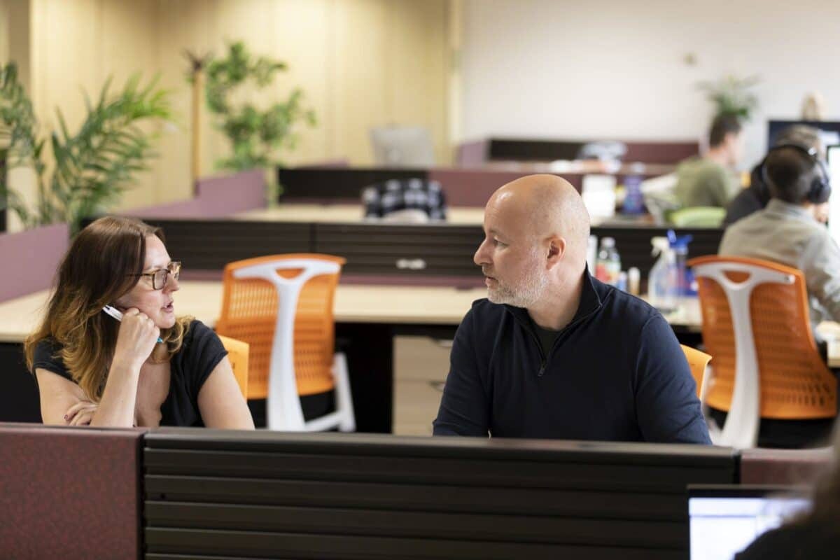 Two members in conversation at their desks