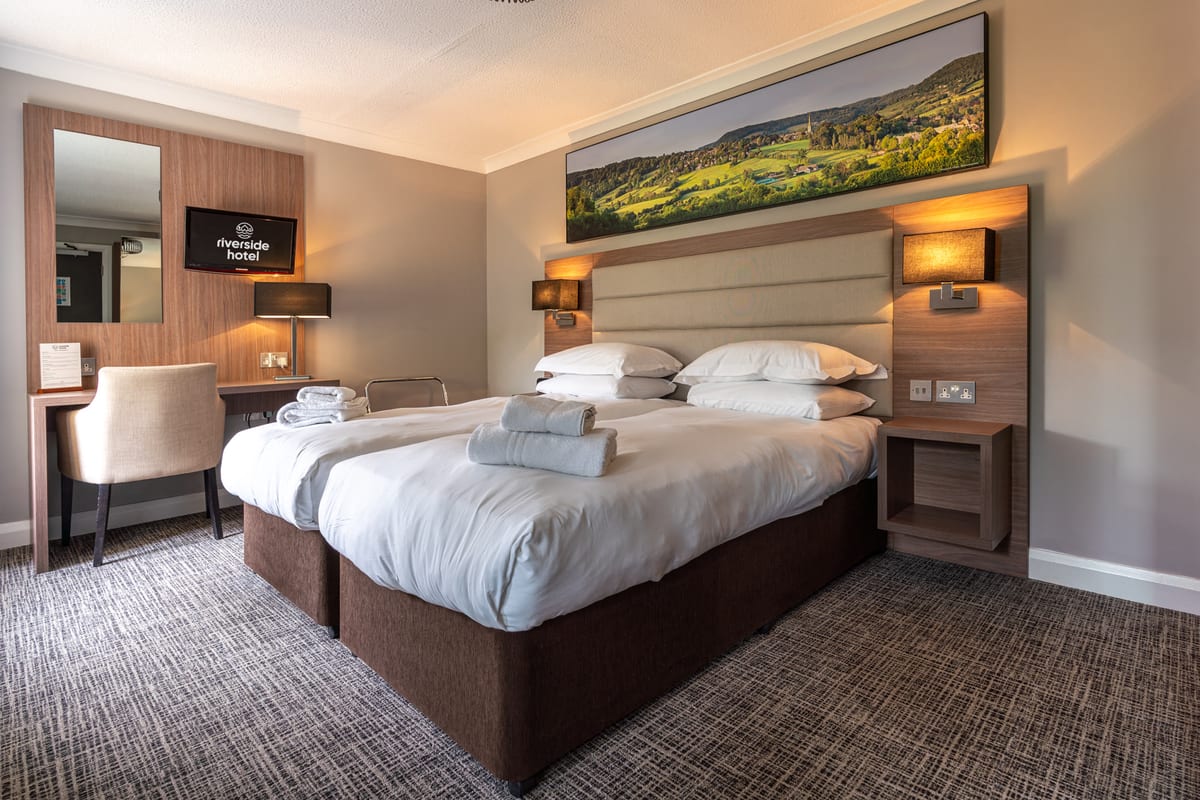 An en-suite hotel room at Riverside with a king bed and Cotswold landscape artwork